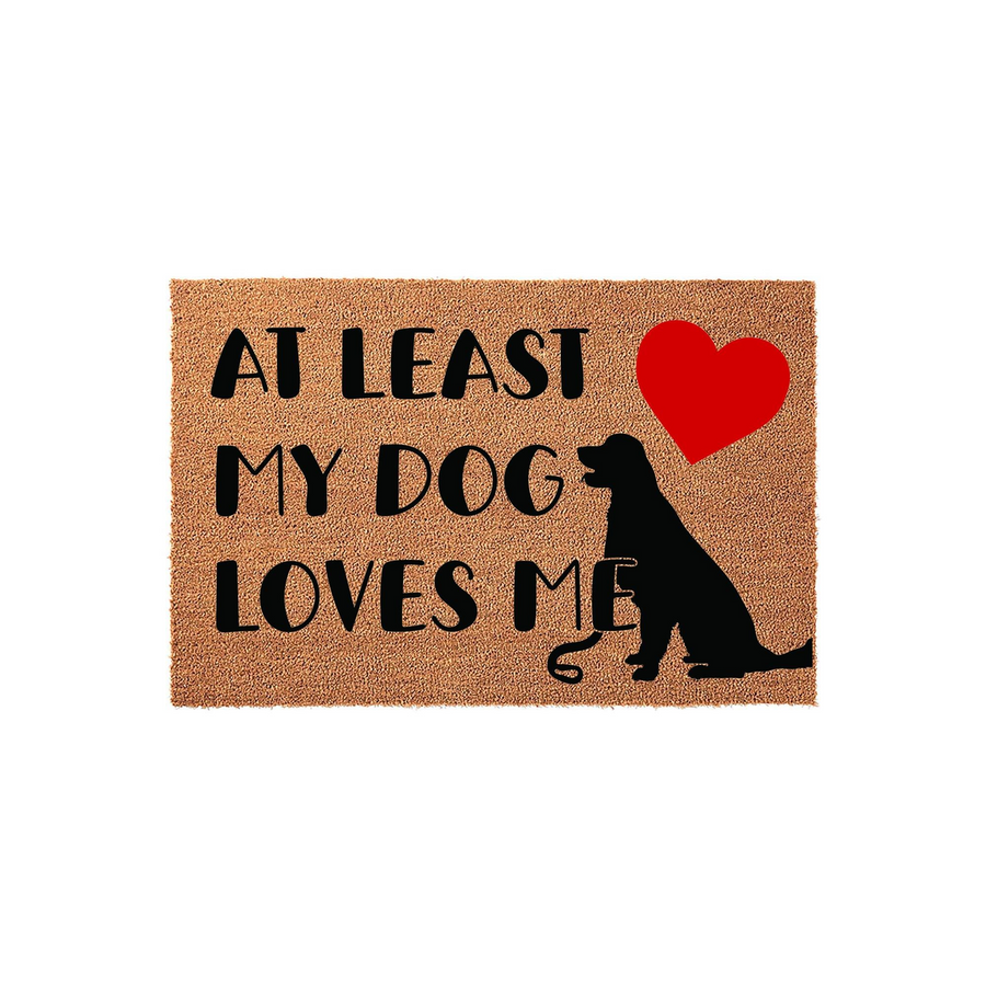 At Least My Dog Loves Me coir doormat featuring a black silhouette of a Labrador Retriever sitting next to a bright red heart, providing a humorous and welcoming entrance decor piece for any dog lover's home on a natural fiber