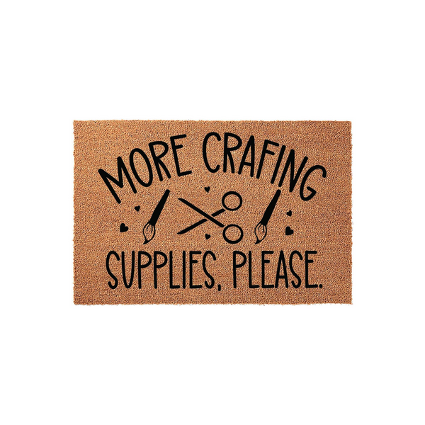 More Crafting Supplies Please doormat made of natural coir fiber, featuring black printed text and icons of scissors and paintbrushes, perfect for a creative hobby room or a crafter's home entrance on a clean white studio