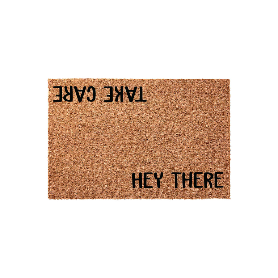 Hey There Take Care coir doormat featuring a natural brown fiber texture with black printed text, designed with a friendly greeting on one side and a parting message on the other for a unique front porch entryway decor statement.