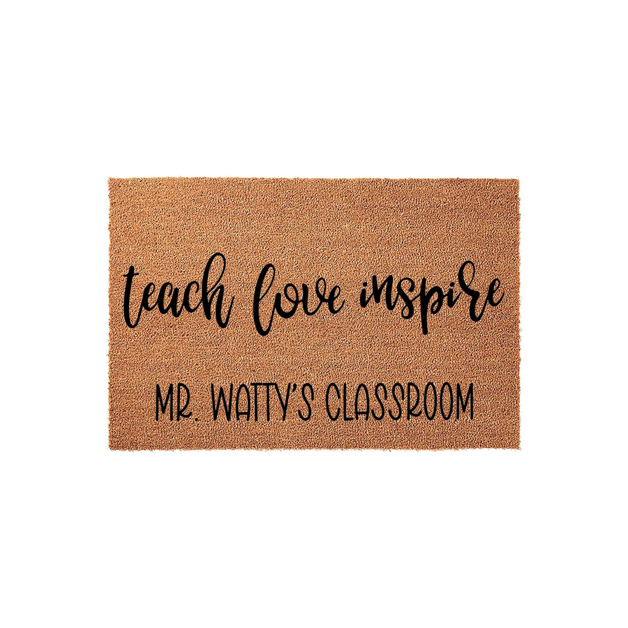 Personalized teacher classroom doormat made of natural coir fiber, featuring the words teach love inspire in black script and a custom name printed in a clean sans-serif font against a plain white studio background for a school