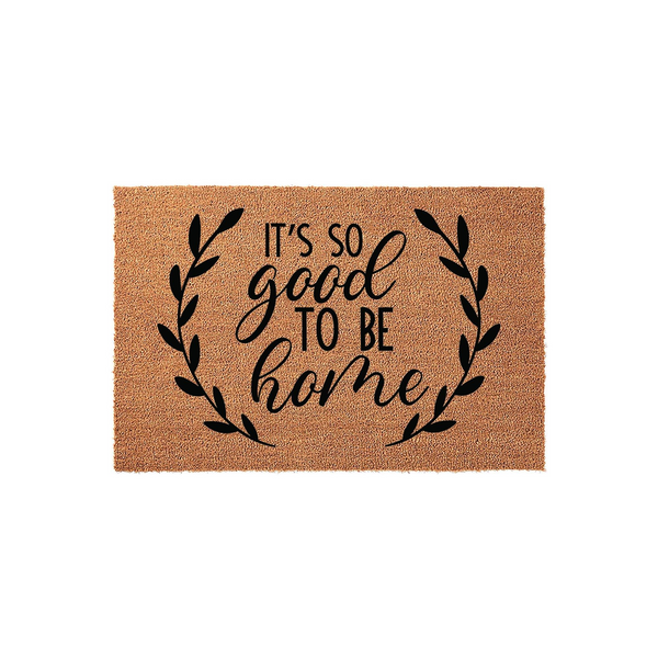 It's So Good To Be Home coir doormat featuring a natural brown fiber texture and black printed text surrounded by a decorative leaf wreath, creating a welcoming entryway accent for any front porch or house entrance.