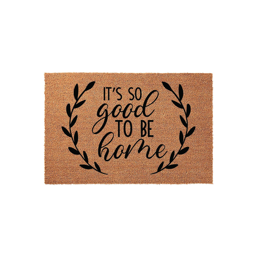 It's So Good To Be Home coir doormat featuring a natural brown fiber texture and black printed text surrounded by a decorative leaf wreath, creating a welcoming entryway accent for any front porch or house entrance.