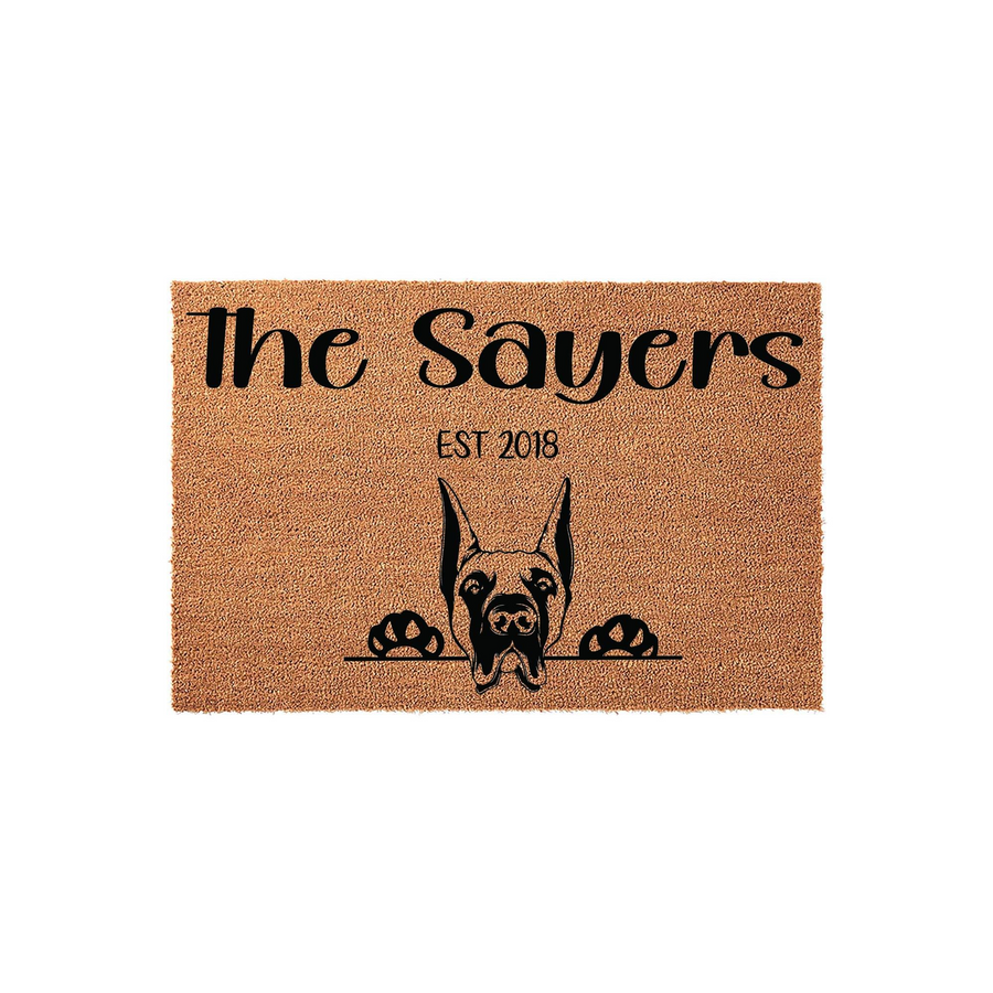 Personalized Doberman Pinscher doormat featuring a natural coir texture with a black graphic of a dog peeking over a line, customized with a family name and established year for a welcoming front porch entrance decor piece.