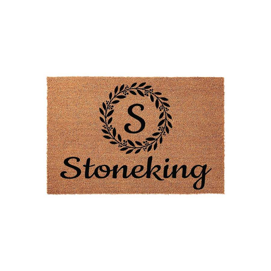Personalized coir doormat featuring a black printed laurel wreath design with a central monogram letter and a custom family name underneath, set against a clean white background for a classic and welcoming home entryway aesthetic.