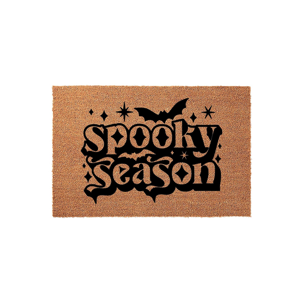 Spooky Season Halloween doormat featuring a natural coir texture with bold black lettering, a flying bat silhouette, and decorative star accents, creating a festive entryway decor piece for the fall holiday season on a plain