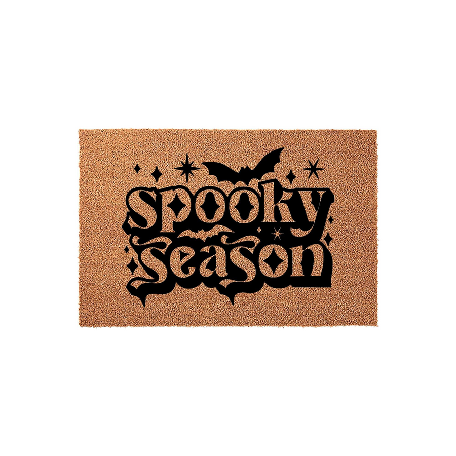 Spooky Season Halloween doormat featuring a natural coir texture with bold black lettering, a flying bat silhouette, and decorative star accents, creating a festive entryway decor piece for the fall holiday season on a plain