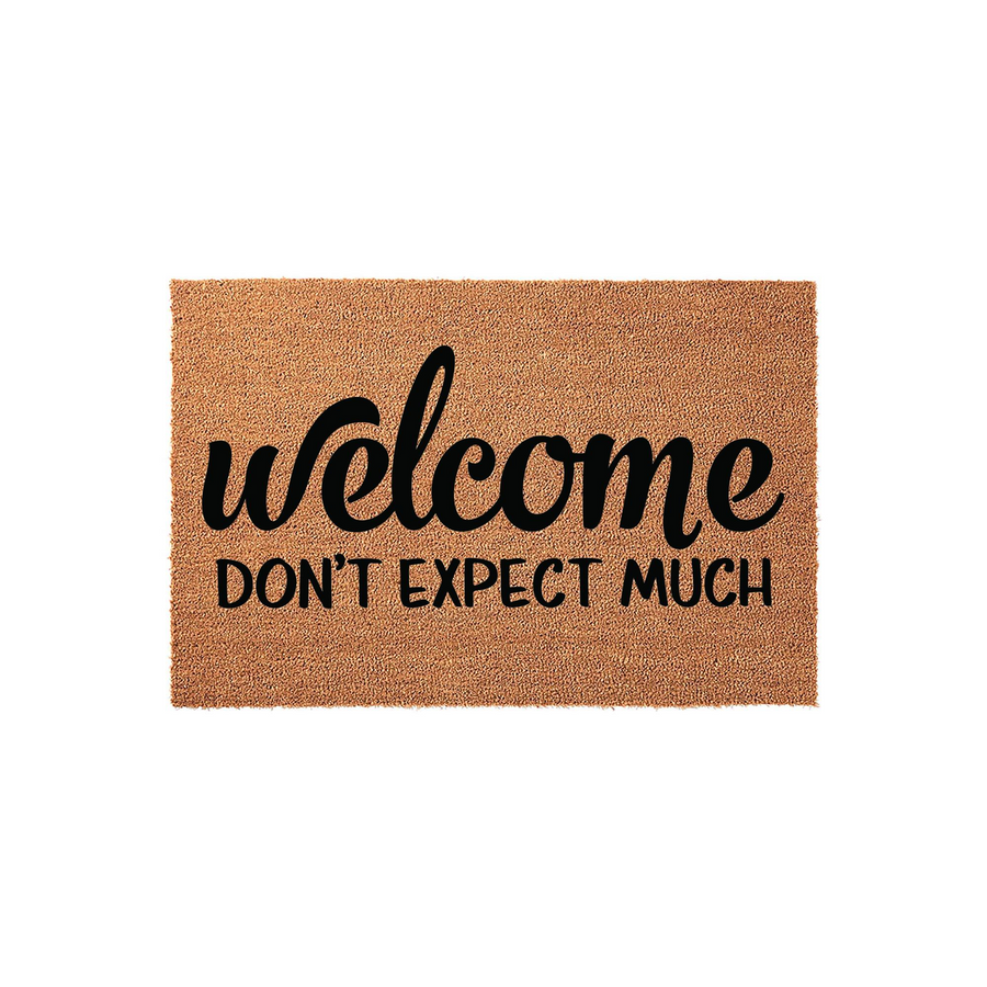 Funny Welcome Don't Expect Much coir doormat featuring bold black typography printed on a natural tan fiber background, creating a humorous and sarcastic entryway decor piece for your front porch or home entrance.