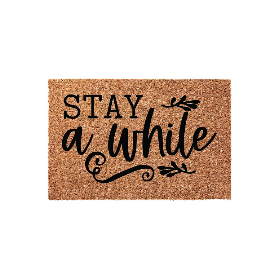 Stay A While Coir Doormat featuring a natural tan fiber texture and bold black lettering with elegant cursive script and decorative leaf accents, creating a welcoming farmhouse style entrance for your front porch or home entryway.
