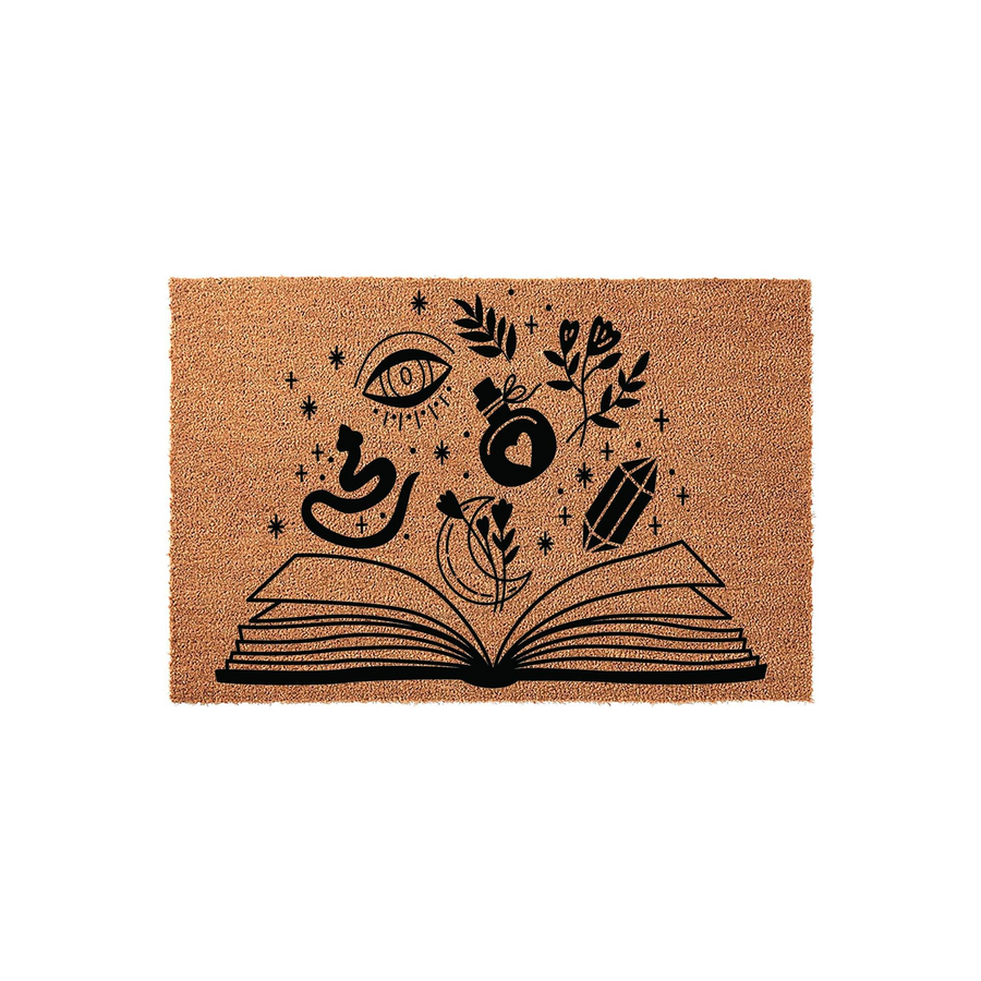 Witchy Book Coir Doormat featuring a black ink illustration of an open book with magical elements like a crystal, potion bottle, snake, and eye floating above it, set against a natural tan fiber background for a mystical home