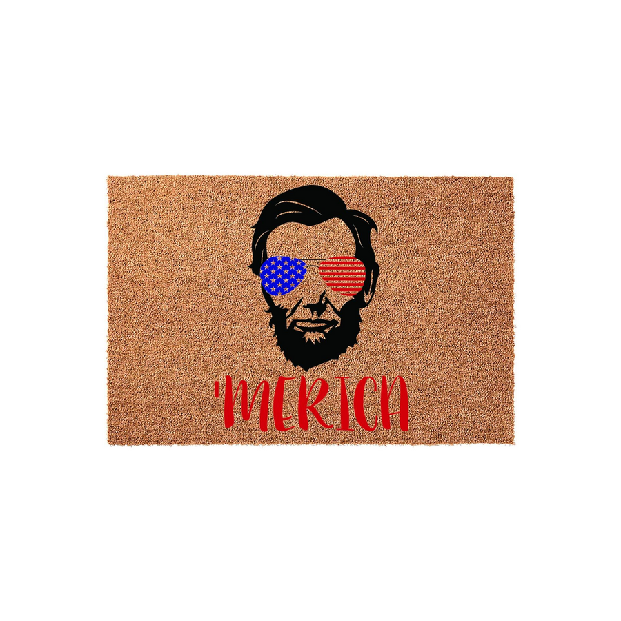 Abraham Lincoln patriotic doormat featuring a graphic of the president wearing American flag sunglasses with the word Merica printed in red below, set against a natural brown coir fiber background for a fun Fourth of July home