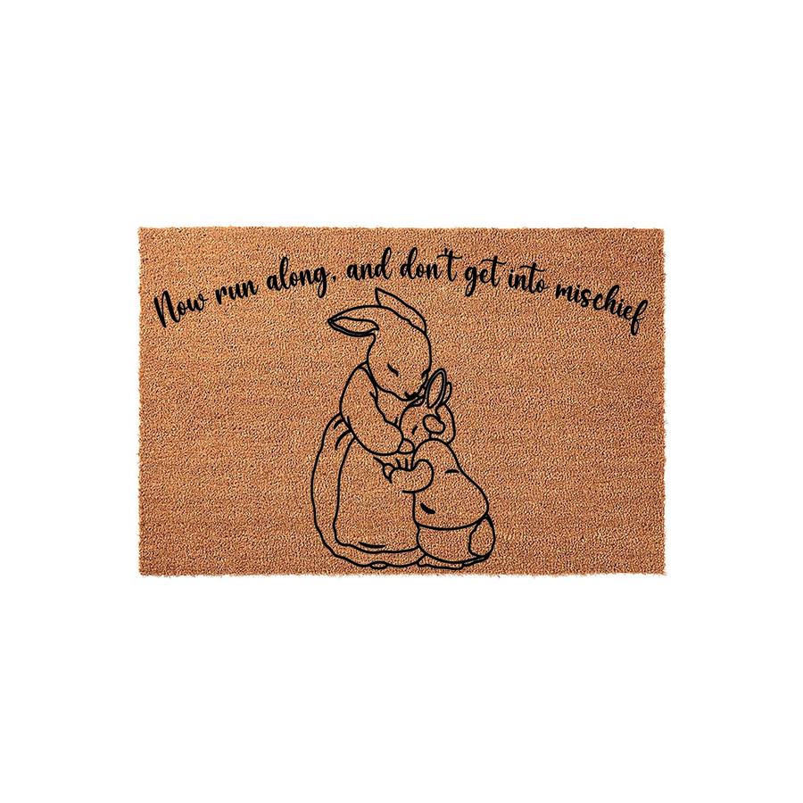 Peter Rabbit themed coir doormat featuring a black line art illustration of a mother bunny hugging her child, with the text Now run along and don't get into mischief printed in a whimsical script font on a natural tan fiber