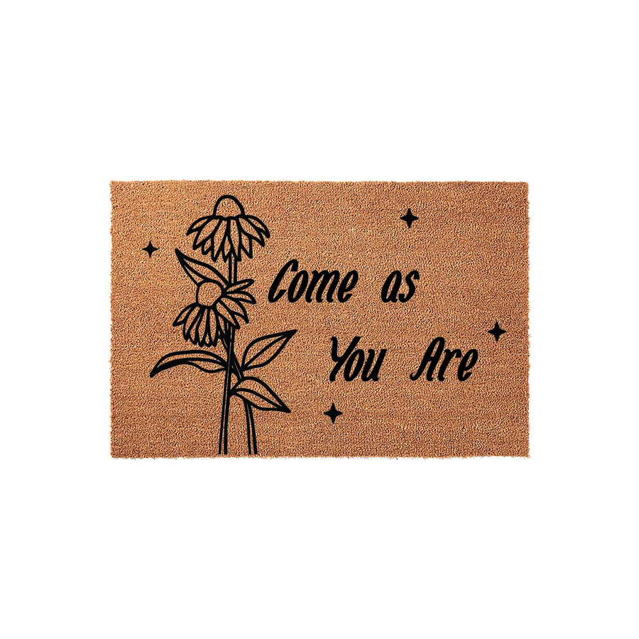 Come as You Are floral coir doormat featuring a black line art illustration of two daisies and small star accents on a natural brown coconut fiber background, creating a welcoming entryway decor piece for your home front porch.