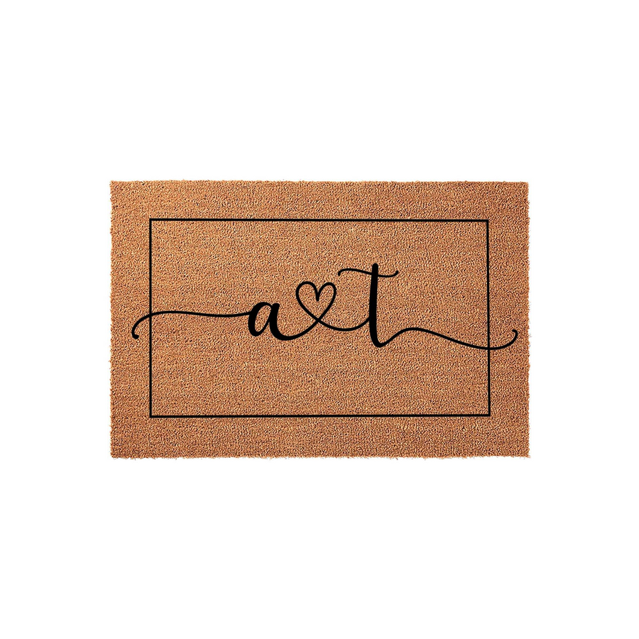 Personalized Coir Doormat featuring a custom monogram design with a heart symbol between two letters, centered inside a thin black rectangular border on a natural brown textured fiber background for a welcoming home entrance.