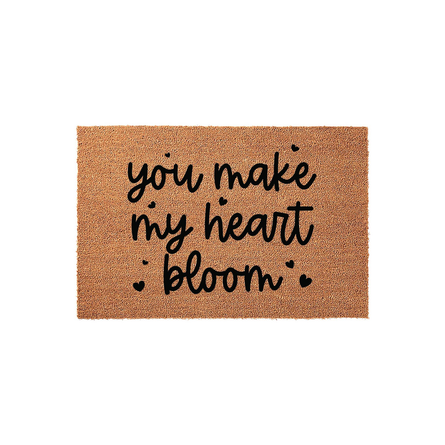 You Make My Heart Bloom coir doormat featuring a natural brown fiber texture and bold black script lettering that reads you make my heart bloom with small heart accents, creating a charming entryway decor piece for a home.