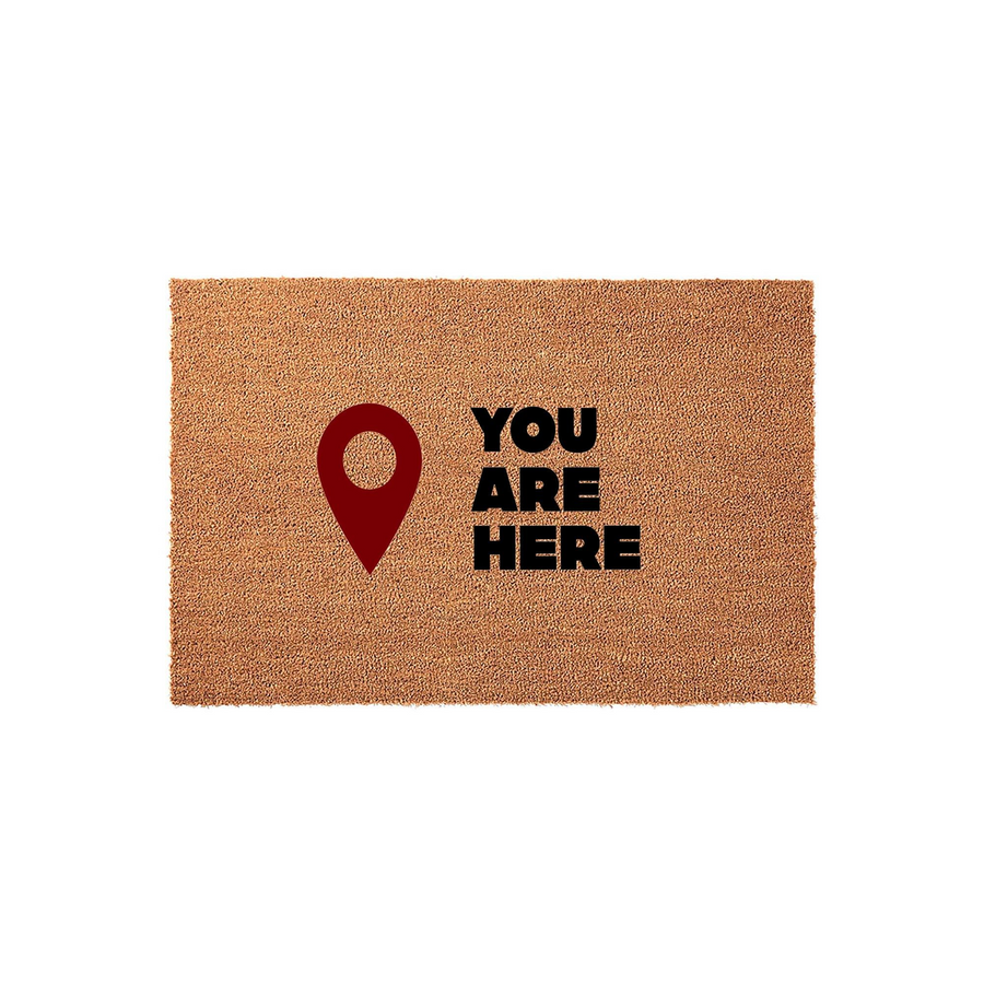 You Are Here coir doormat featuring a bold red map location pin icon next to the black text, providing a humorous and welcoming touch to your front porch entryway with this durable natural fiber outdoor floor mat for your home.