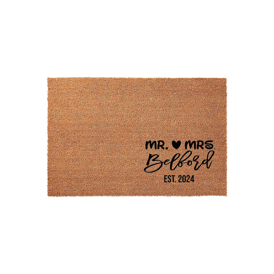 Personalized Mr. and Mrs. wedding doormat featuring a natural coir texture with black printed text that includes a heart icon, a family name, and an established year, making it a charming addition to a newlywed couple's front