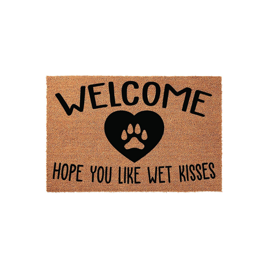 Dog lover welcome doormat made of natural coir fiber, featuring a black heart icon with a paw print in the center and the text Welcome Hope You Like Wet Kisses printed in a bold, playful font against a plain white background.