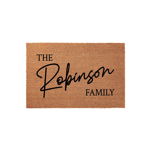 Personalized family name coir doormat featuring a natural brown coconut fiber texture with black printed text that reads The Family in a mix of elegant script and clean serif fonts, perfect for a custom home entryway or front