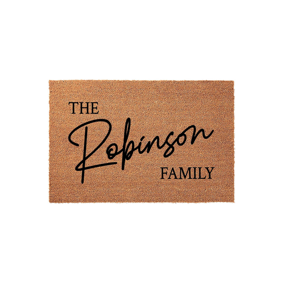Personalized family name coir doormat featuring a natural brown coconut fiber texture with black printed text that reads The Family in a mix of elegant script and clean serif fonts, perfect for a custom home entryway or front