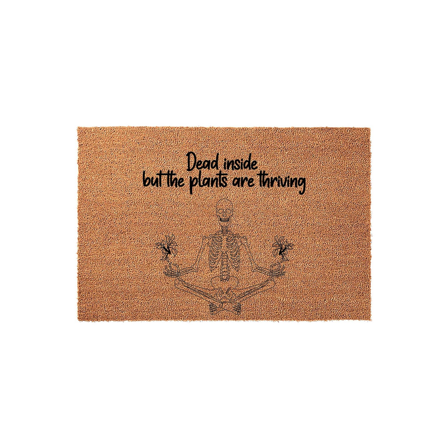 Dead inside but the plants are thriving coir doormat featuring a black line art illustration of a skeleton sitting in a lotus yoga pose, holding small potted plants in its hands against a natural brown textured fiber background.