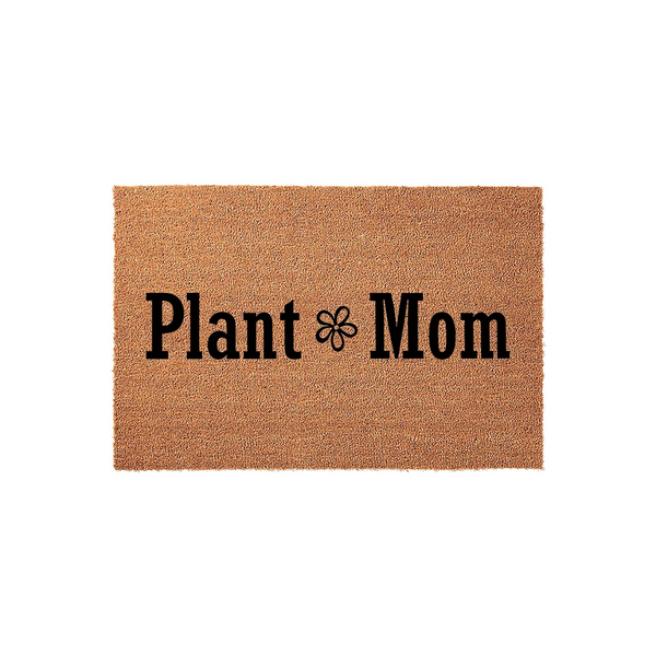 Plant Mom coir doormat featuring a natural tan fiber texture and bold black lettering with a small flower icon in the center, displayed against a clean white background for a modern home entryway or porch decor aesthetic.