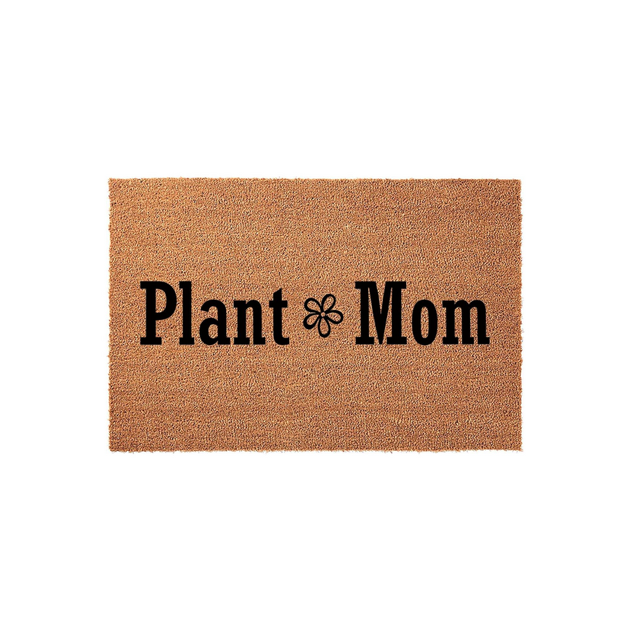 Plant Mom coir doormat featuring a natural tan fiber texture and bold black lettering with a small flower icon in the center, displayed against a clean white background for a modern home entryway or porch decor aesthetic.