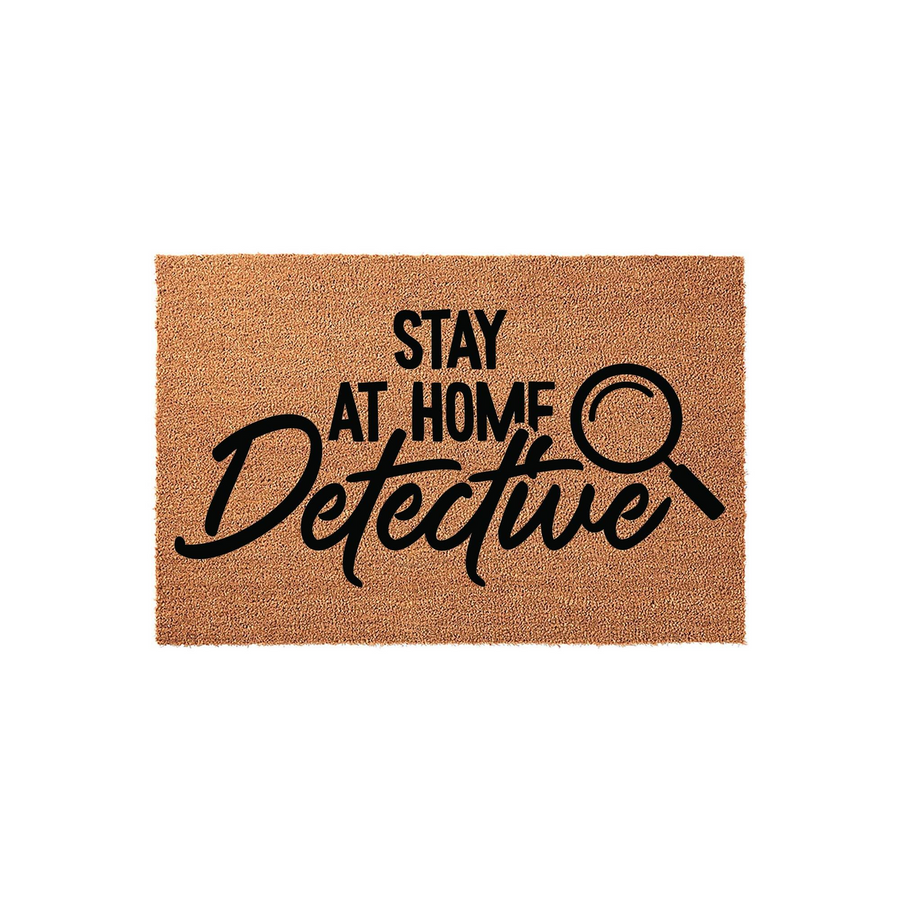 Stay At Home Detective coir doormat featuring a natural brown fiber texture and bold black lettering with a magnifying glass icon, creating a fun and unique entryway floor mat for mystery lovers and home decor enthusiasts.