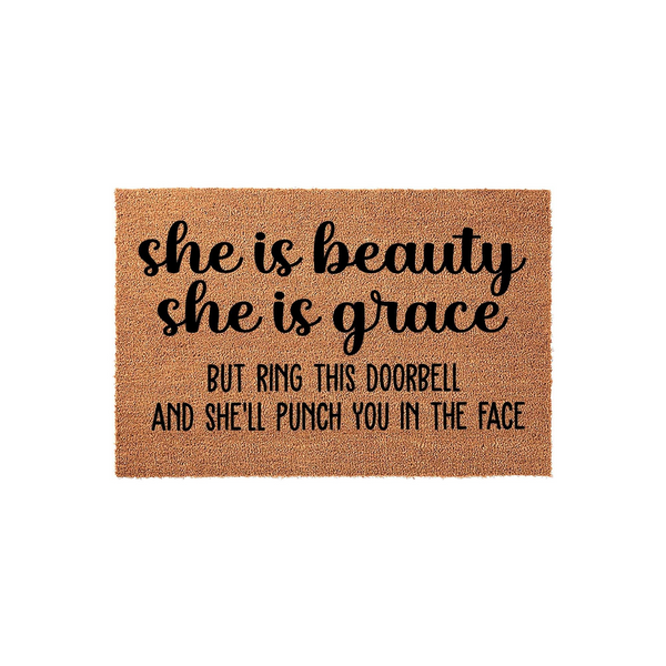 Funny doormat with a natural coir texture featuring the humorous quote she is beauty she is grace but ring this doorbell and she will punch you in the face printed in bold black lettering on a plain white studio background.