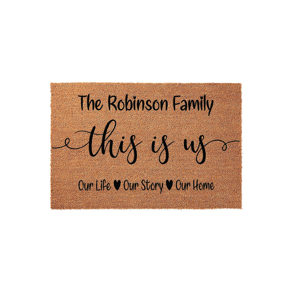 Personalized family name coir doormat featuring the text This Is Us in elegant script, with Our Life, Our Story, and Our Home printed below on a natural brown textured fiber background for a welcoming front porch entrance.
