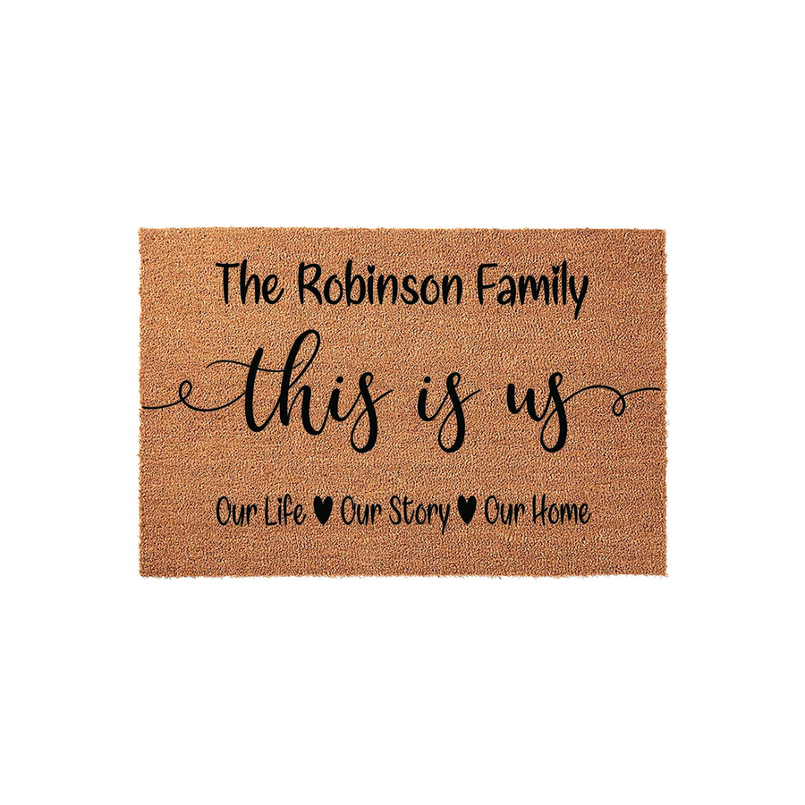 Personalized family name coir doormat featuring the text This Is Us in elegant script, with Our Life, Our Story, and Our Home printed below on a natural brown textured fiber background for a welcoming front porch entrance.