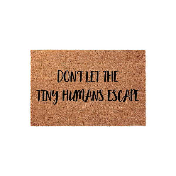 Funny Tiny Humans Escape doormat made of natural coir fiber with a textured brown surface, featuring bold black lettering that warns visitors not to let the kids out, displayed against a clean white studio background for a modern