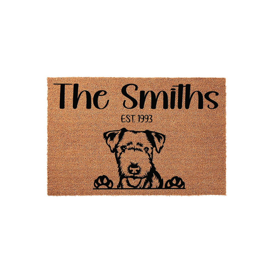 Personalized Airedale Terrier doormat featuring a natural coir texture, custom family name, and established year text printed in black ink above a cute illustration of a dog peeking over the edge with its paws visible on the mat.