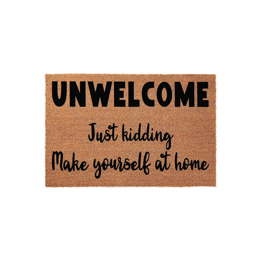 Funny coir doormat featuring the text Unwelcome Just kidding Make yourself at home in bold black lettering, displayed against a clean white background to showcase the natural fiber texture of this humorous front porch entry rug.