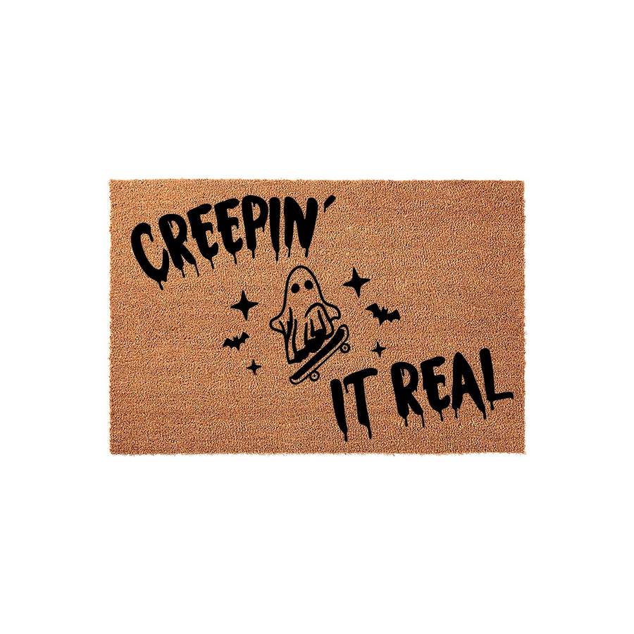 Creepin It Real Halloween doormat featuring a cute ghost riding a skateboard, printed in black ink on a natural tan coir fiber mat, perfect for adding a spooky and fun touch to your front porch decor during the autumn holiday