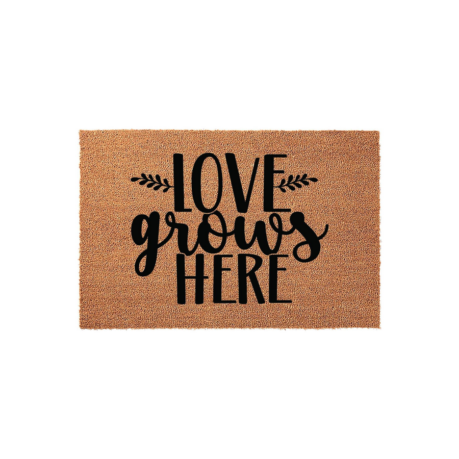 Love Grows Here coir doormat featuring a natural tan fiber texture and bold black lettering with decorative leaf accents, providing a welcoming and rustic farmhouse style touch to your front porch entryway decor.