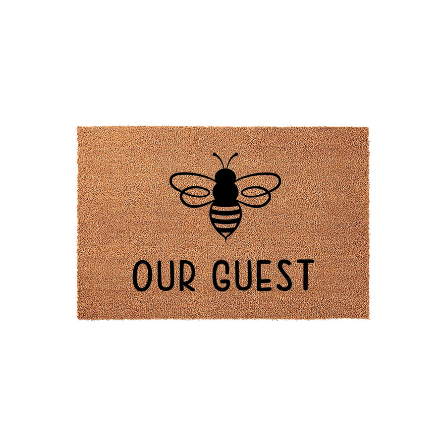 Bee Our Guest doormat featuring a natural coir texture with a black printed bumblebee icon and the playful text Our Guest centered below, creating a charming and welcoming entryway accent for any home front porch or doorstep.