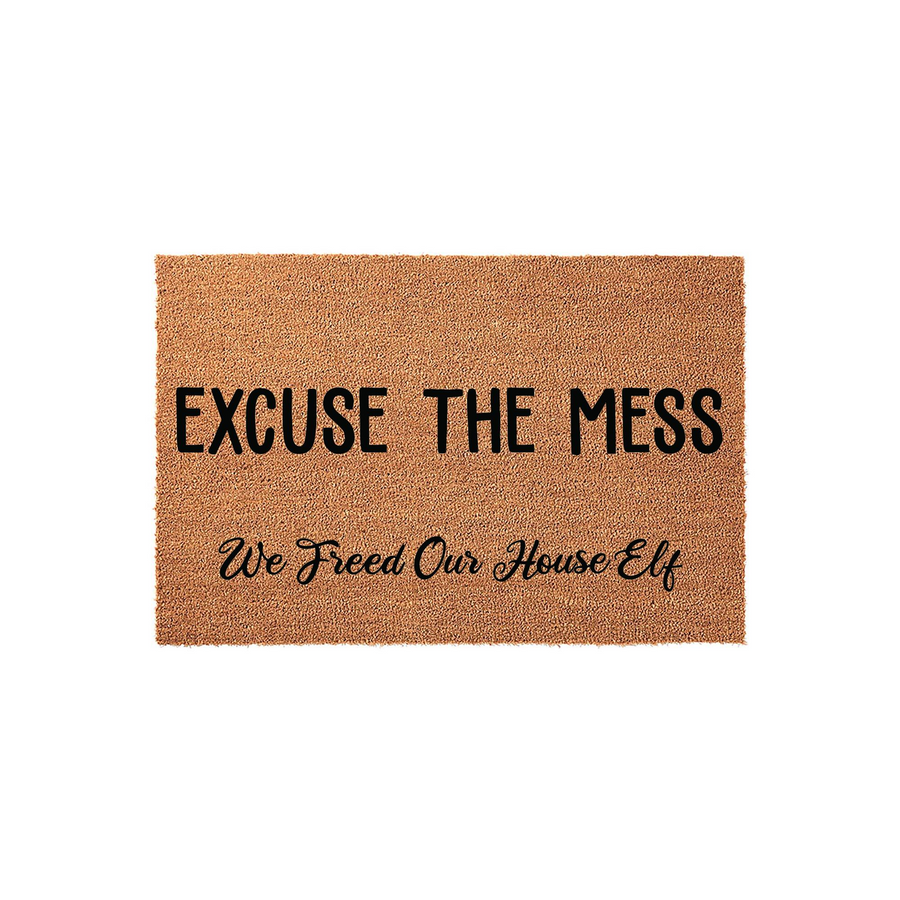Funny Excuse The Mess We Freed Our House Elf coir doormat featuring bold black lettering on a natural tan fiber background, perfect for a whimsical entryway that welcomes guests with a playful pop culture reference to magical