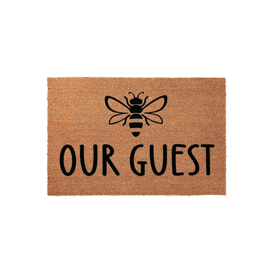 Bee Our Guest coir doormat featuring a natural brown fiber texture with a black printed bumblebee icon and bold lettering centered on the mat, creating a charming and welcoming entrance decor piece for your front porch or home