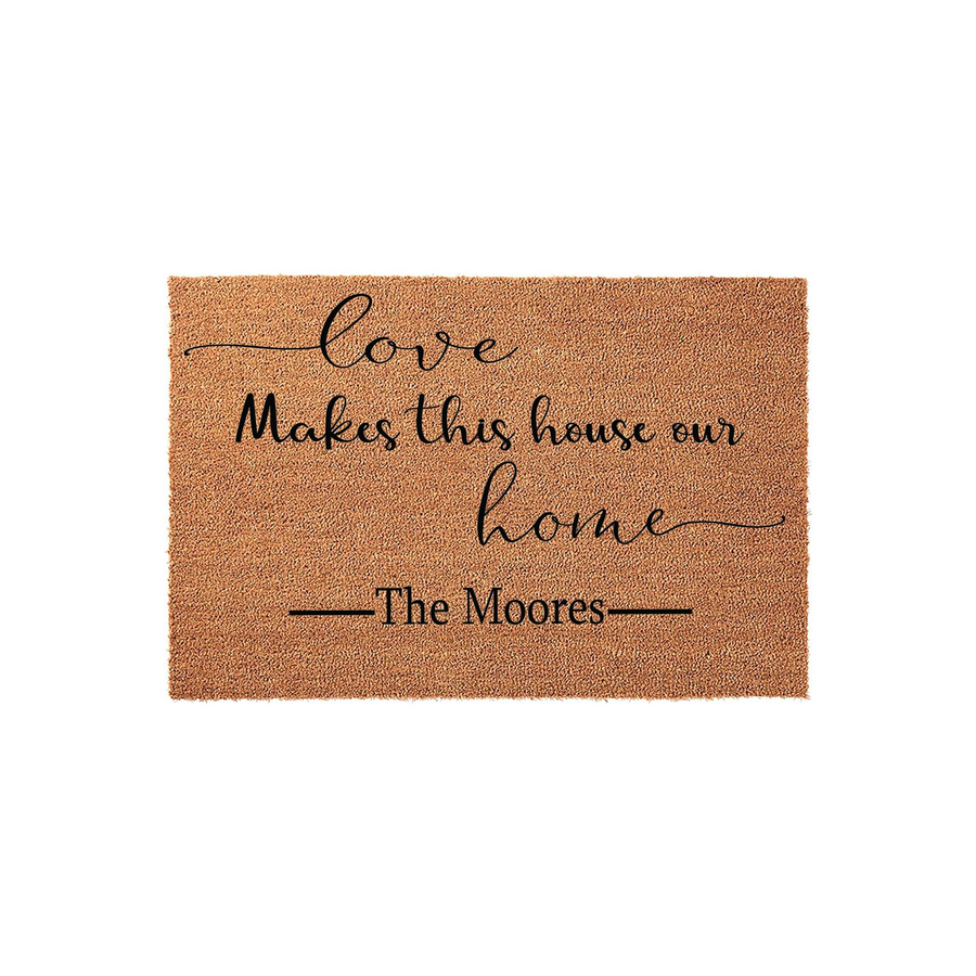 Personalized Family Name Coir Doormat featuring the phrase Love Makes this house our home in elegant black script and serif lettering, centered on a natural brown textured fiber mat for a welcoming front porch entrance decor.