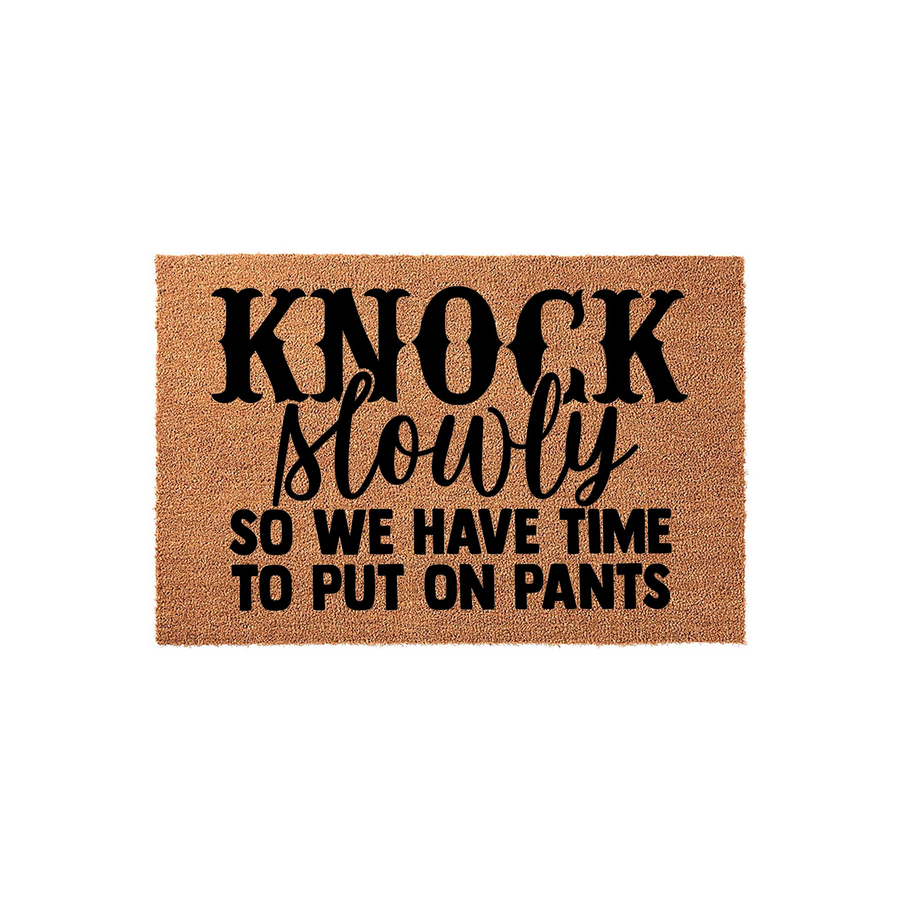 Funny Knock Slowly So We Have Time To Put On Pants doormat featuring bold black typography on a natural tan coir fiber background, creating a humorous and welcoming entrance mat for any home front porch or entryway decor.