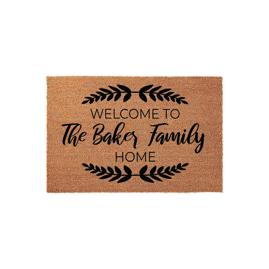 Personalized family name coir doormat featuring a rustic brown texture with black printed text that reads Welcome to the family home, accented by elegant leaf branch designs on a clean white studio background for a modern