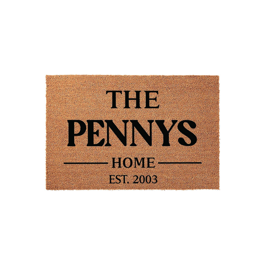 Personalized family name coir doormat featuring a natural tan fiber texture with bold black text that reads The Pennys Home Est. 2003, creating a welcoming entrance piece for a front porch or entryway that celebrates a family