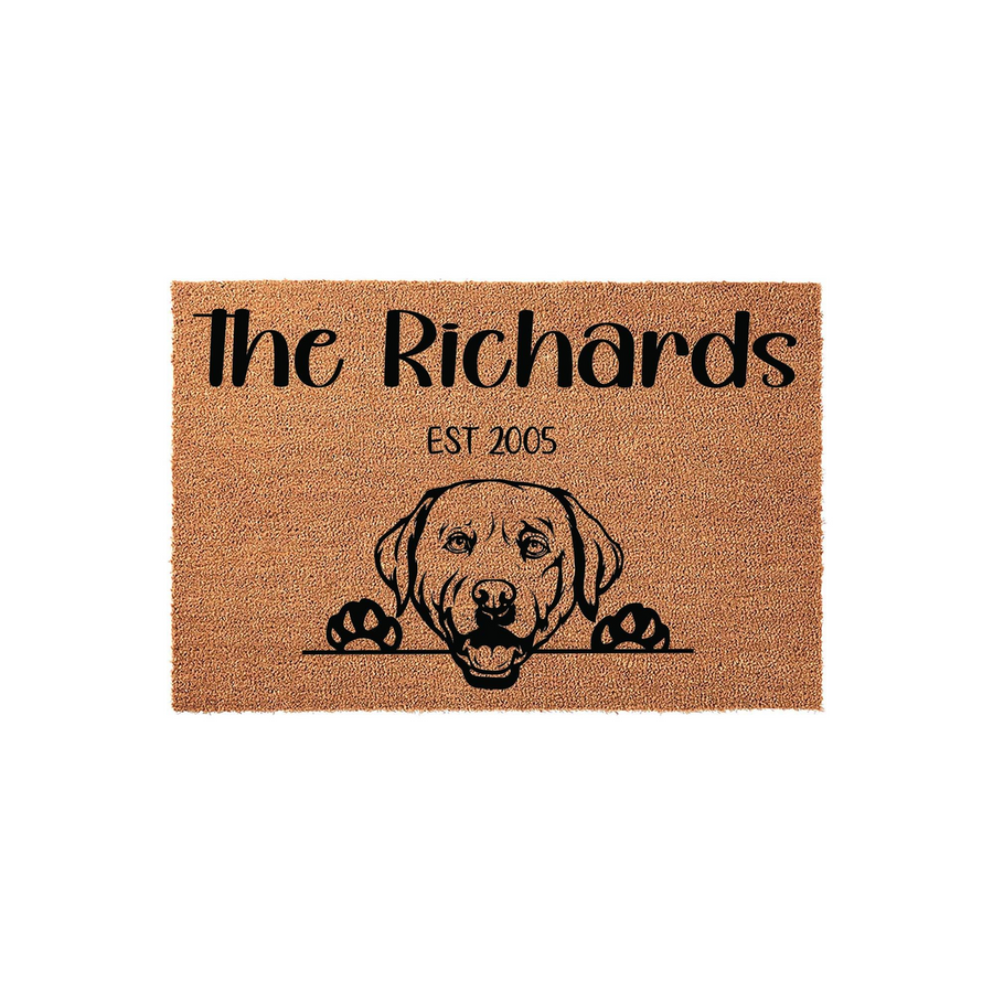 Personalized Labrador Retriever doormat featuring a cute dog illustration peeking over a line, with custom family name text and established year printed on a natural coir fiber mat against a clean white studio background.