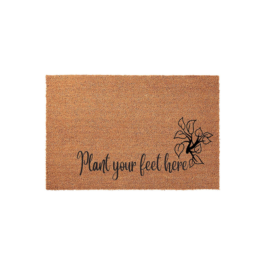 Plant Your Feet Here coir doormat featuring a natural tan fiber texture and black script lettering, accented by a simple botanical leaf illustration on the right side for a charming and welcoming front porch entryway decor.