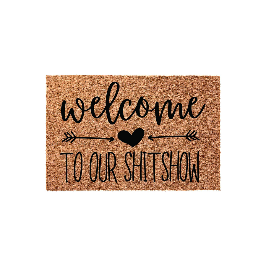 Funny Welcome To Our Shitshow doormat made of natural coir fiber, featuring bold black typography, a central heart icon, and decorative arrows on a plain white background for a humorous front porch entryway decor statement piece.