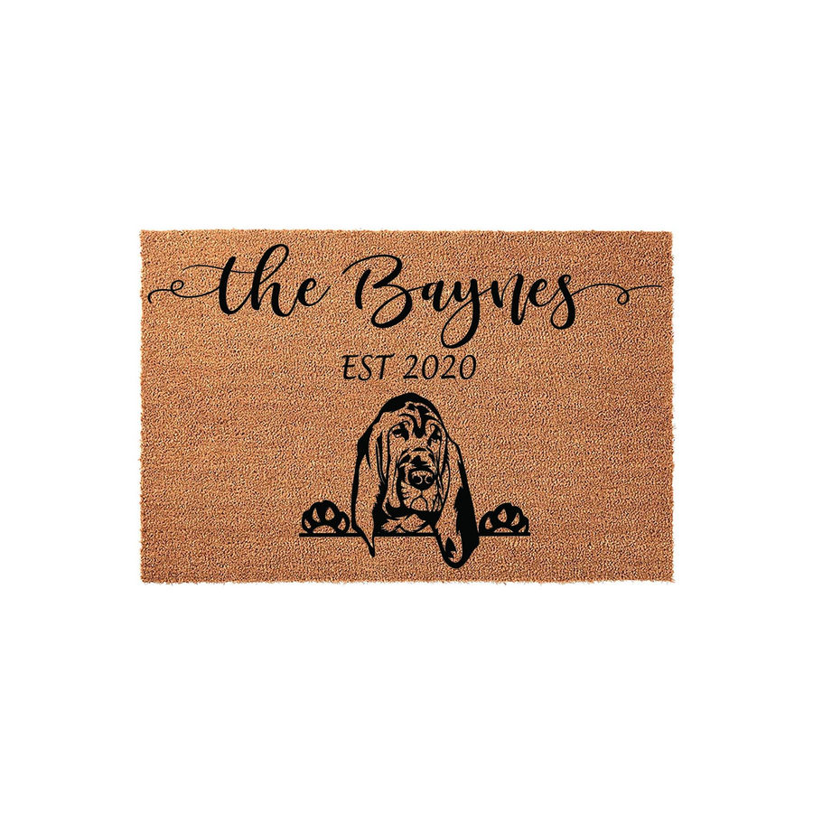 Personalized Basset Hound coir doormat featuring a custom family name and established year in elegant black script, showcasing a cute dog peeking over the bottom edge on a natural tan textured fiber background for a welcoming