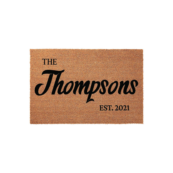 Personalized family name coir doormat featuring a natural brown fiber texture with black printed text that displays a family name and an established year, creating a welcoming entrance for any home on a clean white background.
