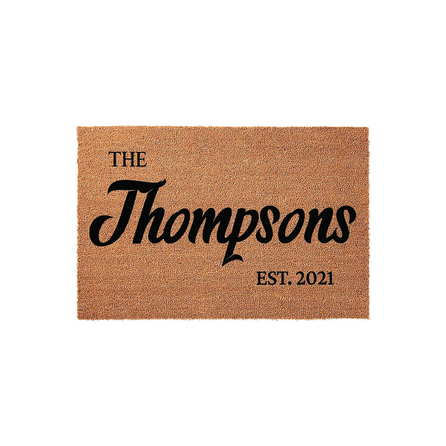Personalized family name coir doormat featuring a natural brown fiber texture with black printed text that displays a family name and an established year, creating a welcoming entrance for any home on a clean white background.