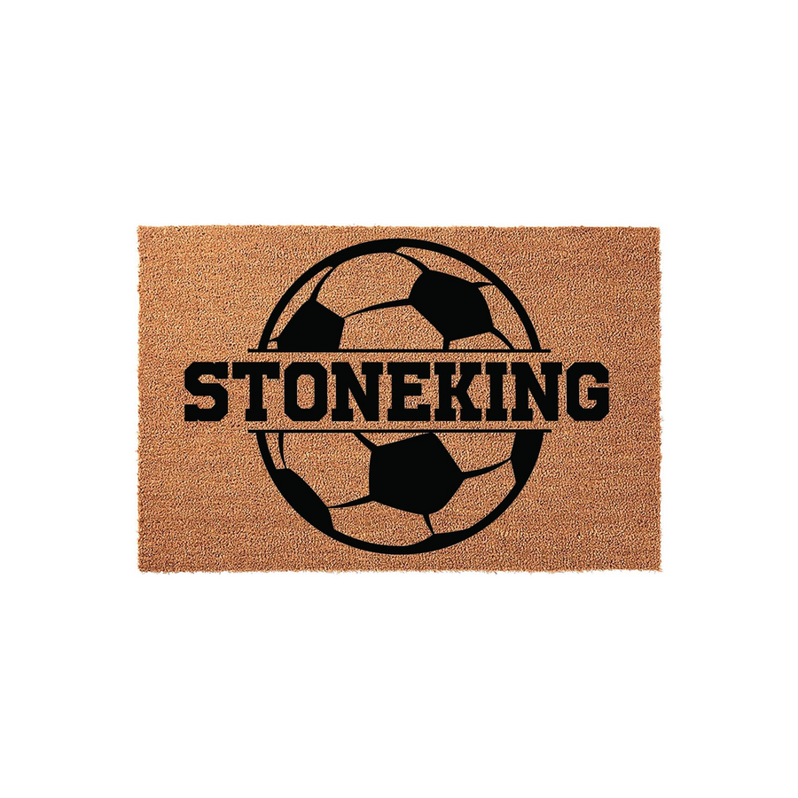 Personalized soccer ball doormat featuring a large black graphic of a soccer ball with a horizontal split across the center for a custom family name, set against a natural tan coir fiber background for a sporty outdoor entryway