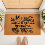 Happiness Is Being A Grandma coir doormat featuring floral line art, placed at a front door entrance as a decorative welcome mat for a grandmother, providing a stylish and functional home decor accent for any porch or entryway.